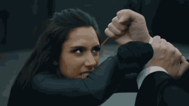 a woman in a black suit is holding a man 's fist in her face