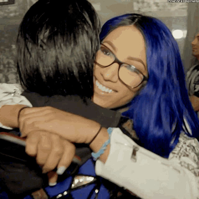 a woman with blue hair is hugging another woman wearing glasses