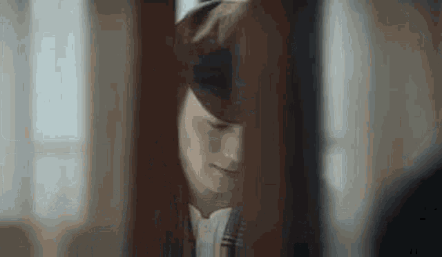 a man in a hat is standing behind a wooden door .