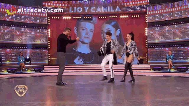 a man and a woman are dancing on a stage with a screen behind them that says eltrecetv.com