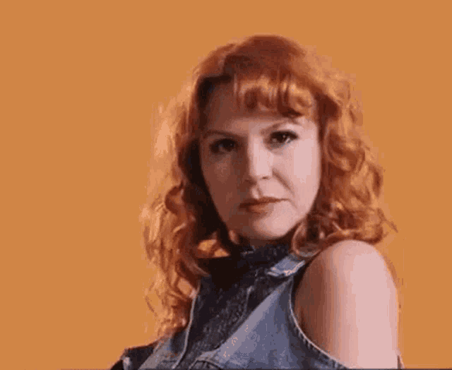 a woman with red hair is wearing a denim vest .