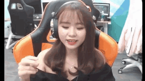 a woman is sitting in an orange gaming chair wearing headphones and a necklace .