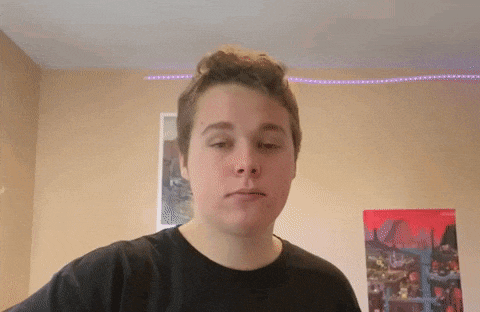 a young man in a black shirt is making a funny face in front of a picture on the wall .