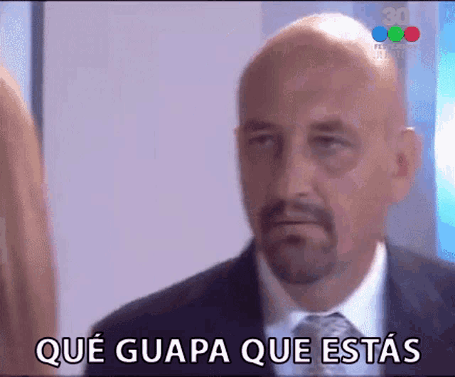 a bald man with a beard is wearing a suit and tie and has the words que guapa que estas above him