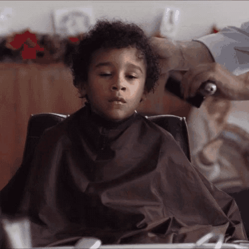 a young boy is getting his hair cut by a barber .