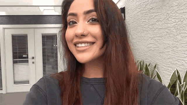 a woman with long brown hair and a nose ring is smiling