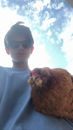 a man wearing sunglasses holds a brown chicken on his lap