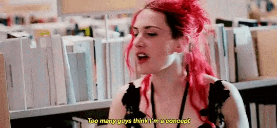 a woman with red hair is standing in front of a bookshelf talking .