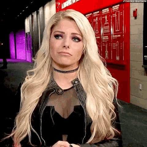 a woman wearing a choker and a leather jacket is standing in front of a red wall .