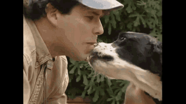 a man in a hat is kissing a dog on the nose .