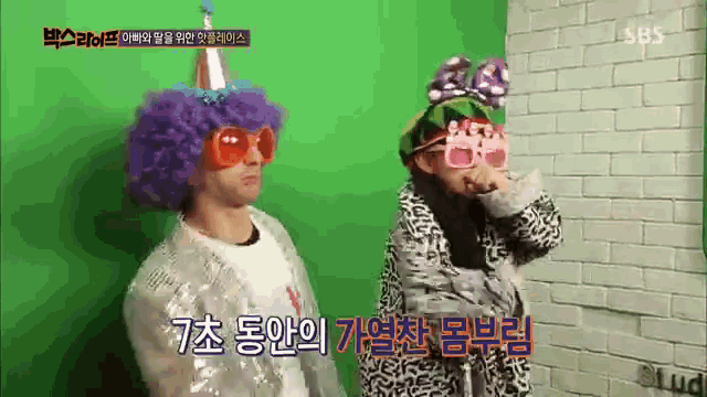 a man in a purple wig is standing next to a woman wearing pink glasses and a party hat .