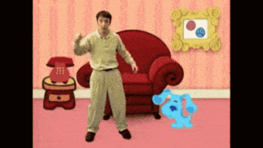 a man is standing in front of a red chair and a blue dog in a living room .