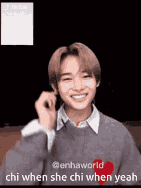a young man is smiling and holding his hand to his ear while wearing a grey sweater .