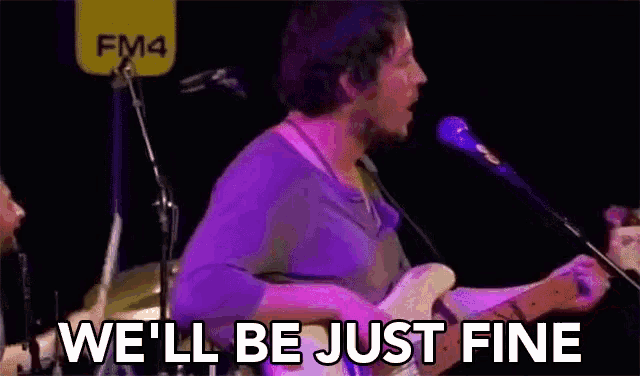 a man is playing a guitar and singing into a microphone while another man stands behind him .
