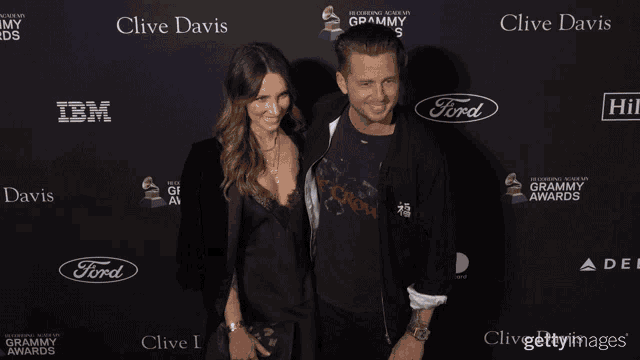 a man and a woman are standing in front of a clive davis advertisement