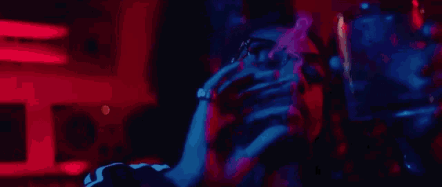a man is smoking a cigarette and drinking a glass of wine in a dark room with red and blue lights .