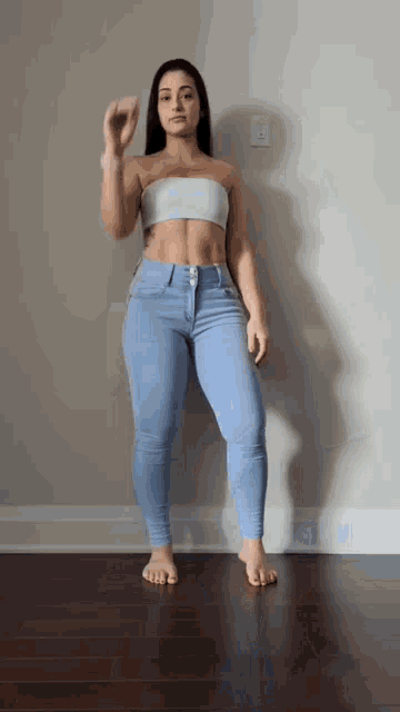 a woman in a crop top and jeans is standing on a wooden floor and giving a thumbs up .