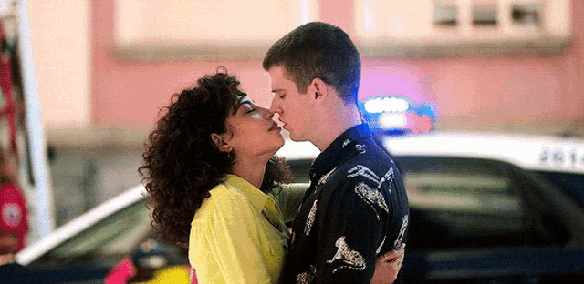 a man and woman are kissing in front of a police car .