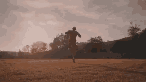 a person is running in a field at sunset with trees in the background .