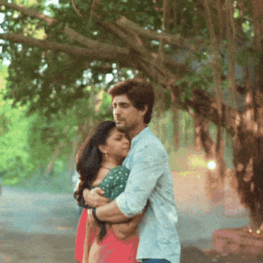 a man and a woman hugging each other in front of a tree