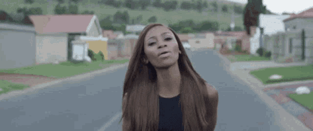 a woman with long hair is standing on the side of a road in a residential area .