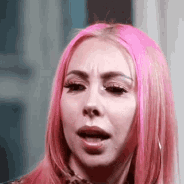 a woman with pink hair is making a funny face and looking at the camera .