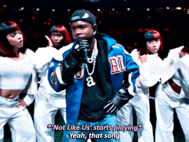 a man in a blue jacket with the letter r on it is singing into a microphone
