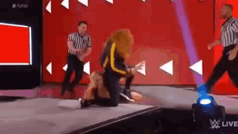 a wrestler is kneeling down on the floor during a match while a referee looks on .