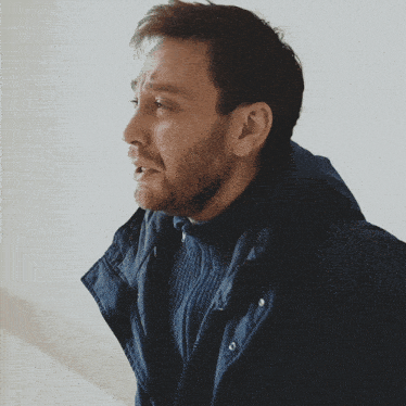 a man with a beard wearing a blue jacket and sweater