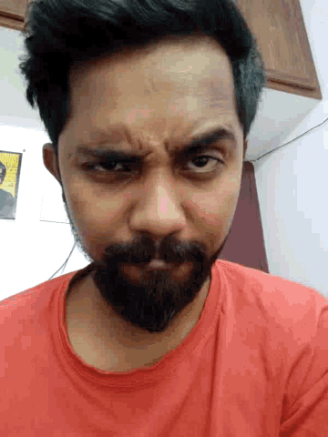 a man with a beard is wearing a red shirt and making a funny face