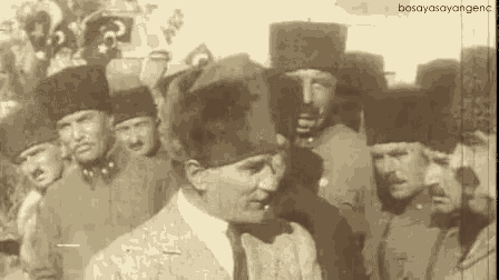 a man in a suit and tie is standing in front of a group of men wearing hats .