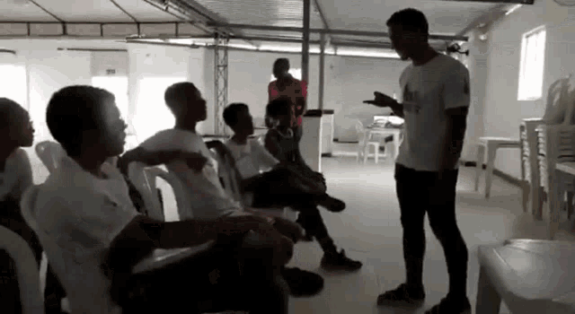 a group of young men are sitting in chairs and talking to a man in a white shirt
