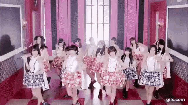 a group of young women are dancing in a hallway in a pink room .