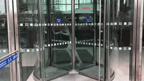 a woman is walking through a revolving glass door with a sign on the side that says ' open '