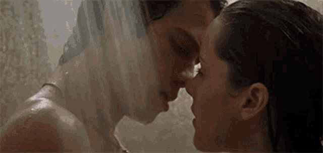 a man and a woman are kissing under a shower head .