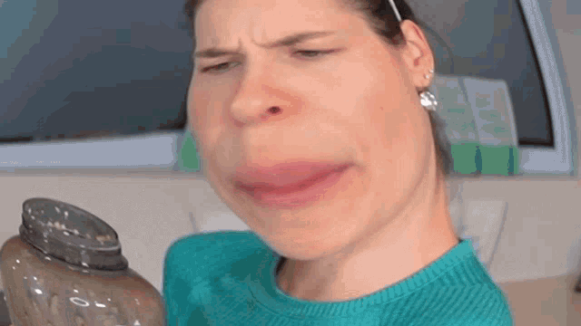 a woman in a blue sweater is making a funny face while holding a water bottle .