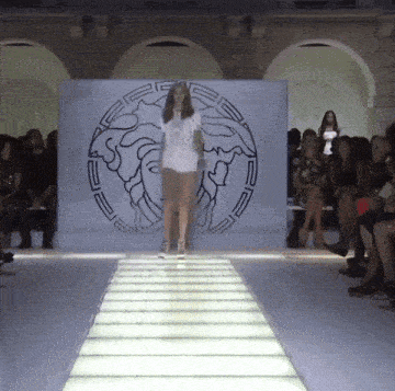a woman is walking down a runway in front of a wall with a medusa on it