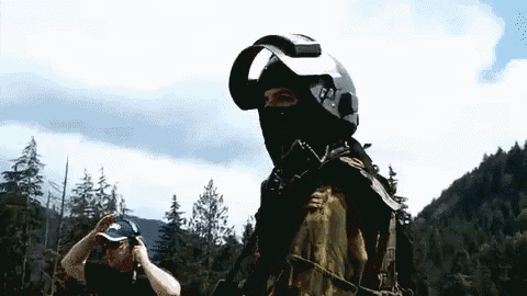 a man wearing a mask and a helmet is standing in a forest