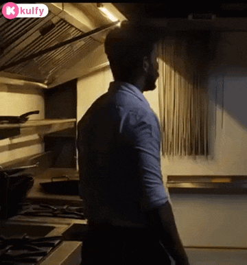 a man in a blue shirt is standing in a kitchen cooking .