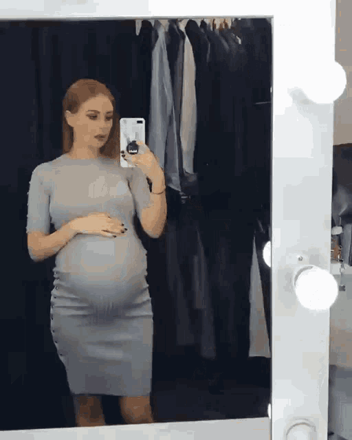 a pregnant woman taking a selfie in front of a mirror