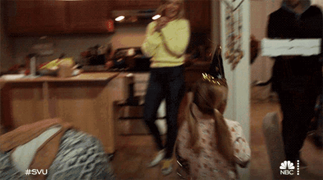 a woman in a yellow sweater is talking on a cell phone while a girl in a party hat looks on