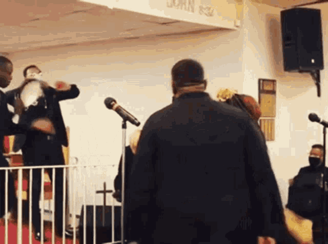 a man in a black jacket stands in front of a microphone in front of a wall that says john 8:32