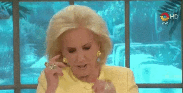a woman in a yellow suit is sitting in front of a window and talking on a phone .