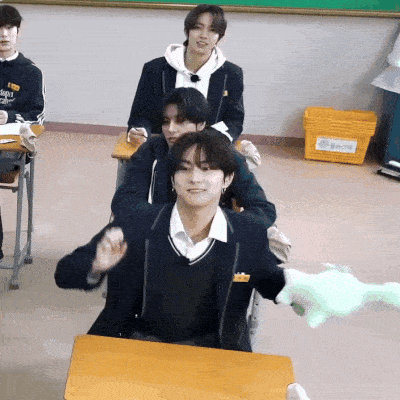 a group of young men are sitting at desks in a classroom and one of them is wearing a black jacket that says angels
