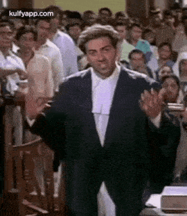 a man in a suit and wig is giving a speech in front of a crowd of people .