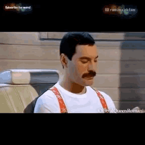 a man with a mustache is sitting in a car with suspenders on .