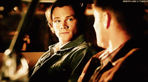 two men are sitting in a car and one of them is looking at the other .