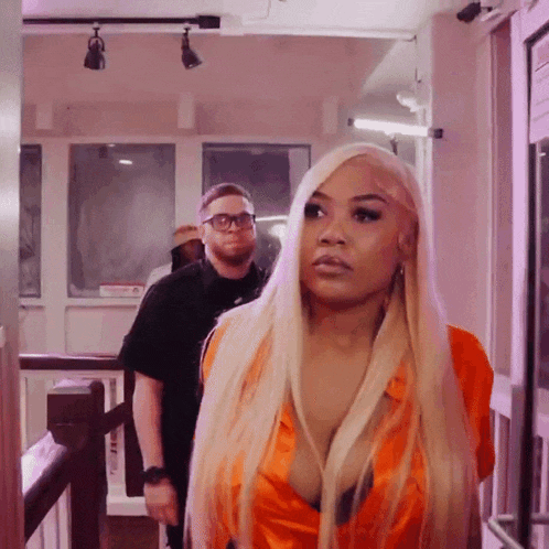a woman with long blonde hair is standing in a hallway with a man behind her