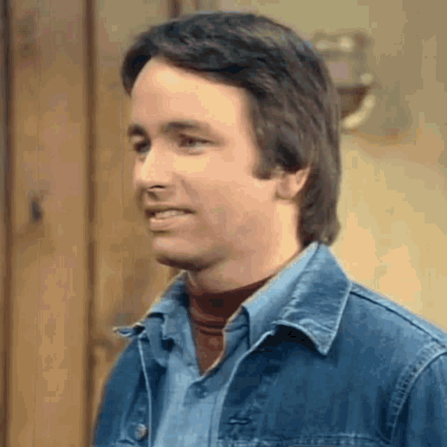 a man in a denim jacket and a red turtleneck is smiling .