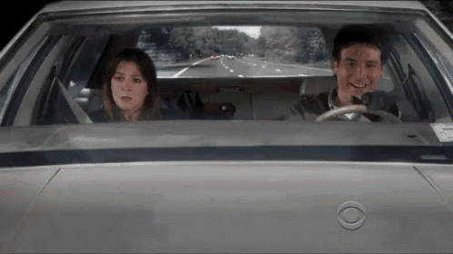 a man and a woman are sitting in a car looking out the window .